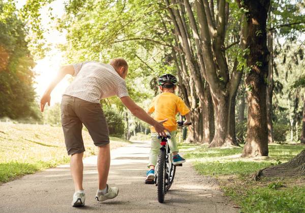 dad teaching child how to ride bicycle